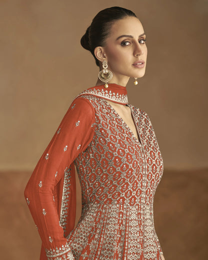 Woman wearing a red and white patterned outfit with gold jewelry against a brown background