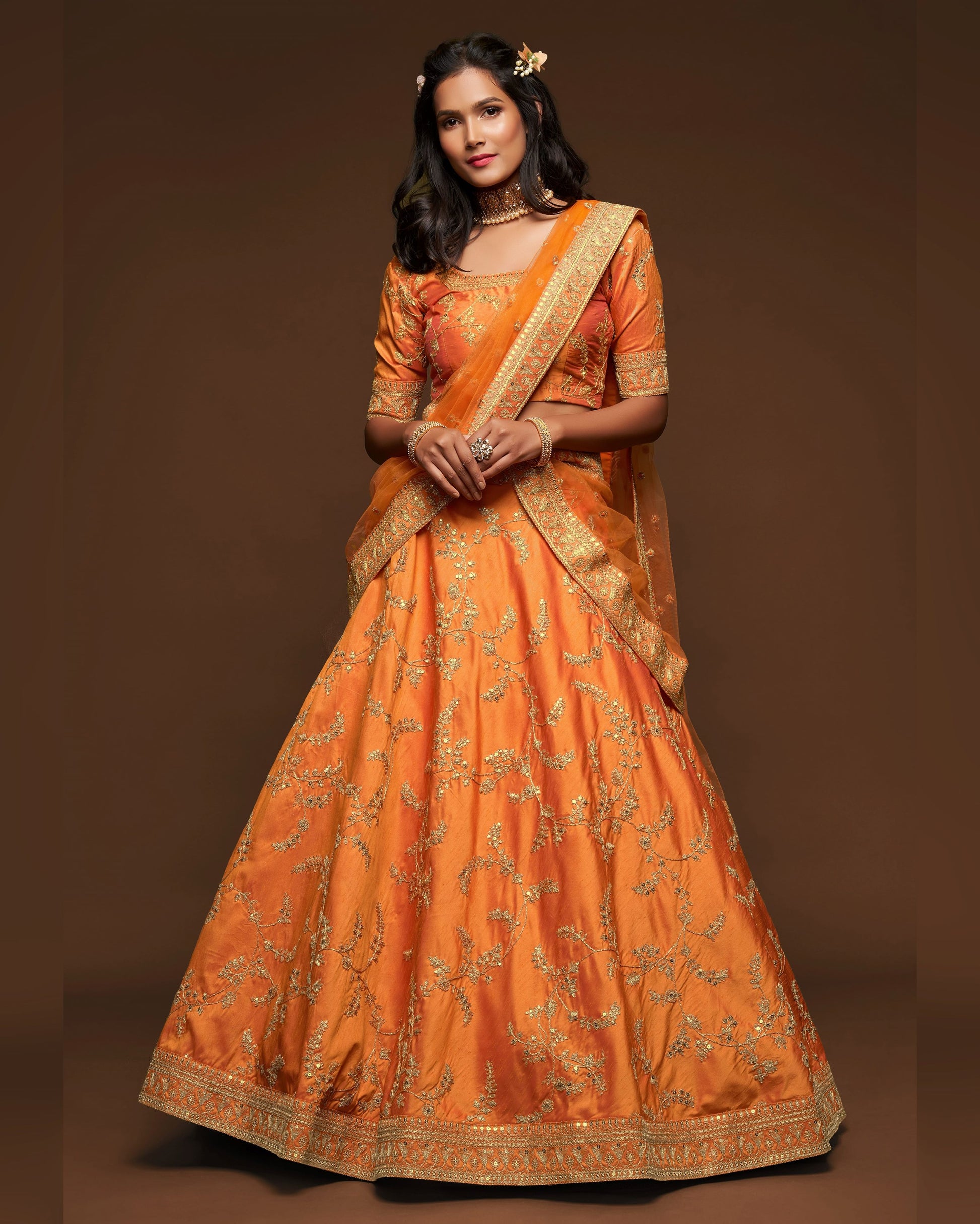 Woman wearing an orange traditional outfit with gold embroidery on a brown background