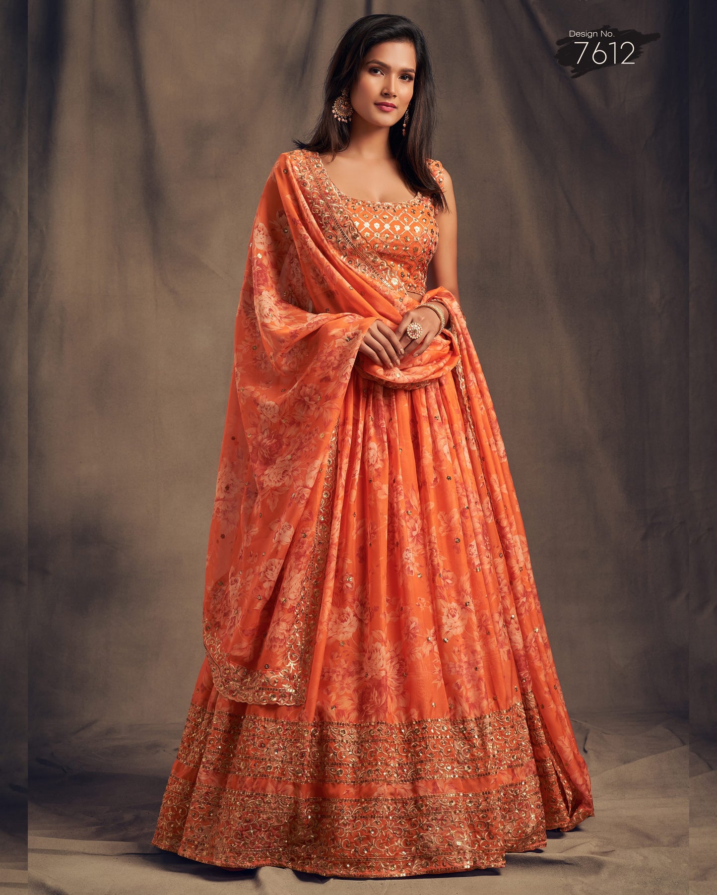 Woman wearing an orange saree with gold patterns against a plain background