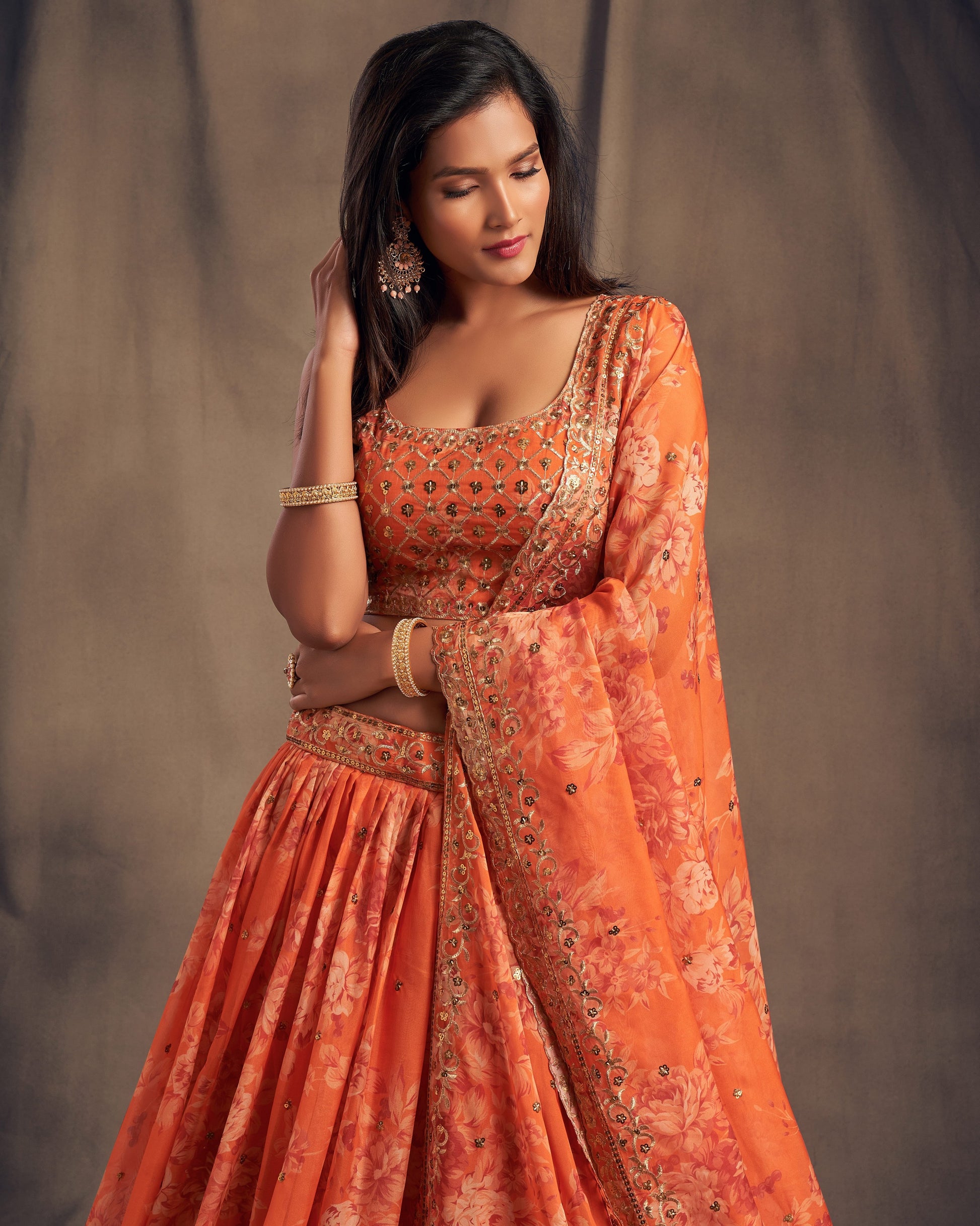 Woman wearing an orange traditional outfit with intricate patterns against a neutral background