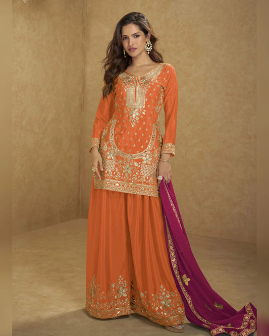 Woman wearing an orange embroidered traditional outfit with a purple dupatta on a beige background