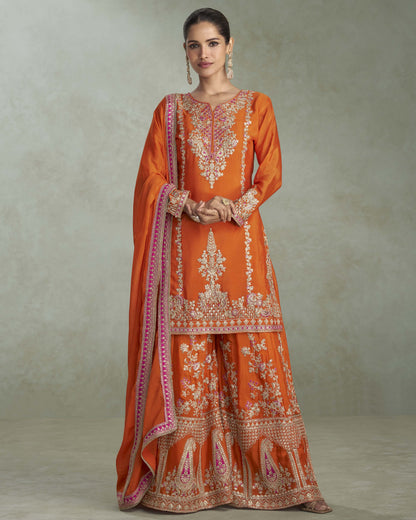 Woman wearing an orange embroidered traditional outfit against a plain background