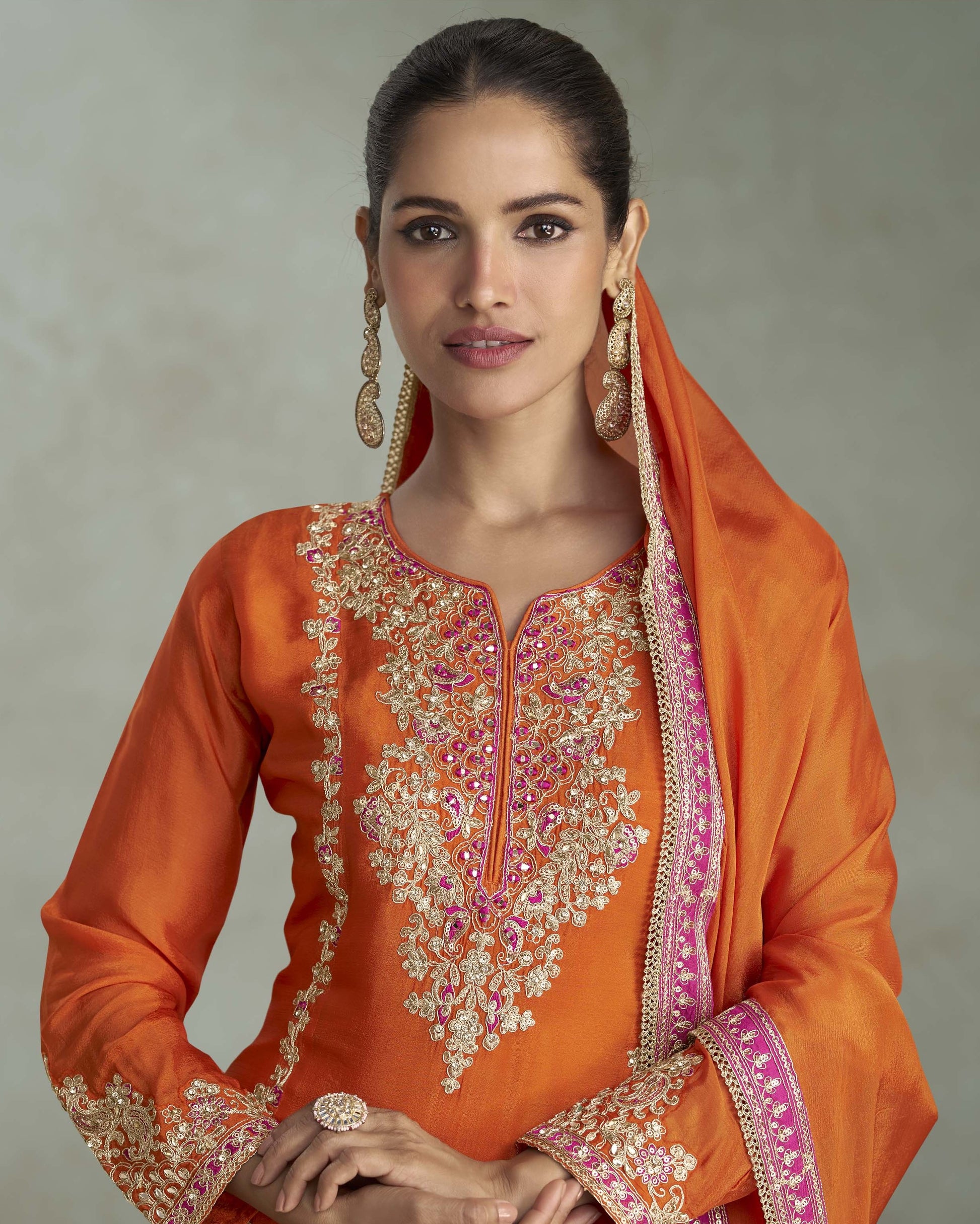 Woman wearing an orange embroidered traditional outfit with a plain background