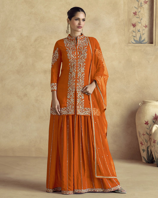 Woman wearing an orange traditional outfit with embroidery in a room setting.