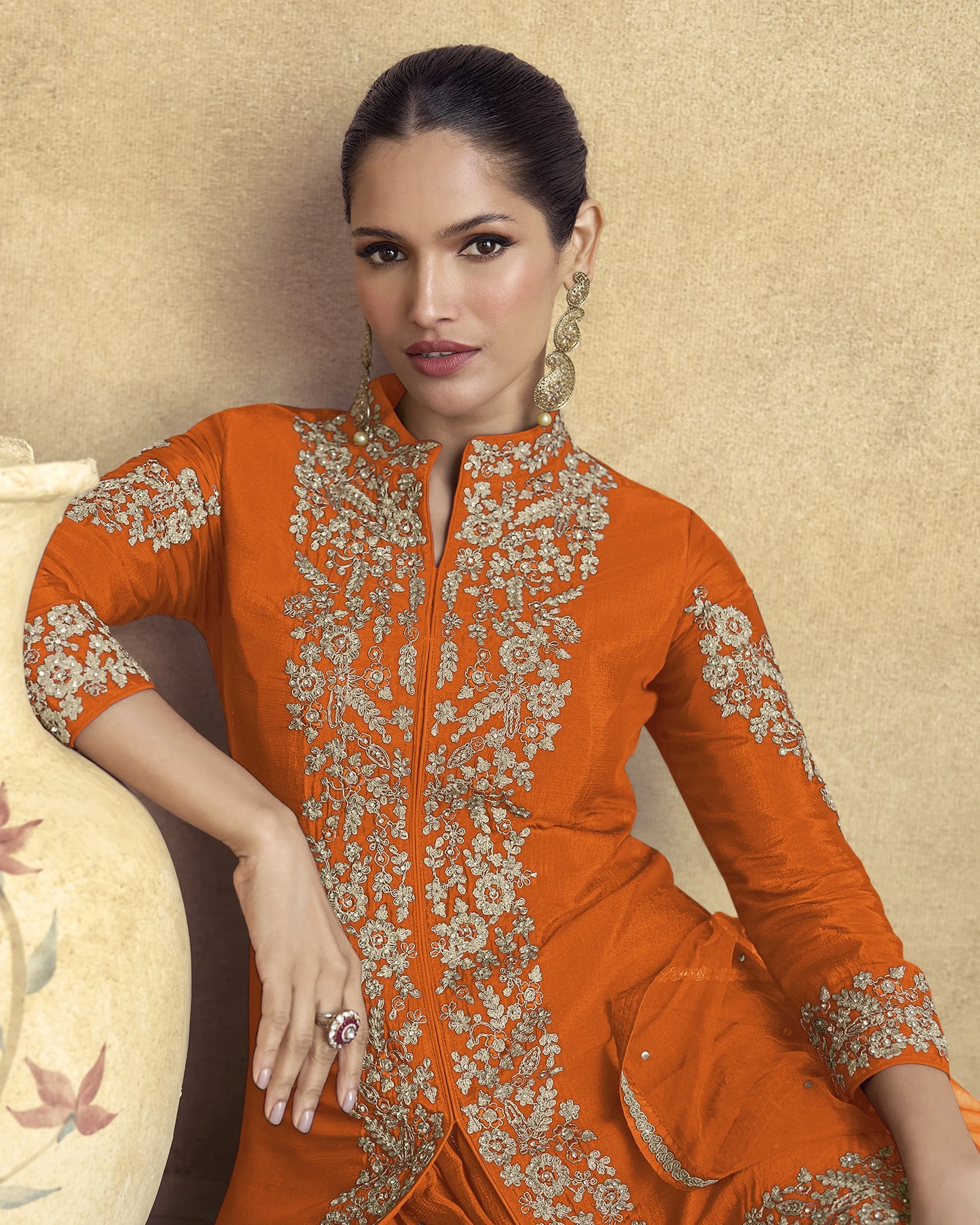 Woman wearing an orange embroidered traditional outfit against a beige background