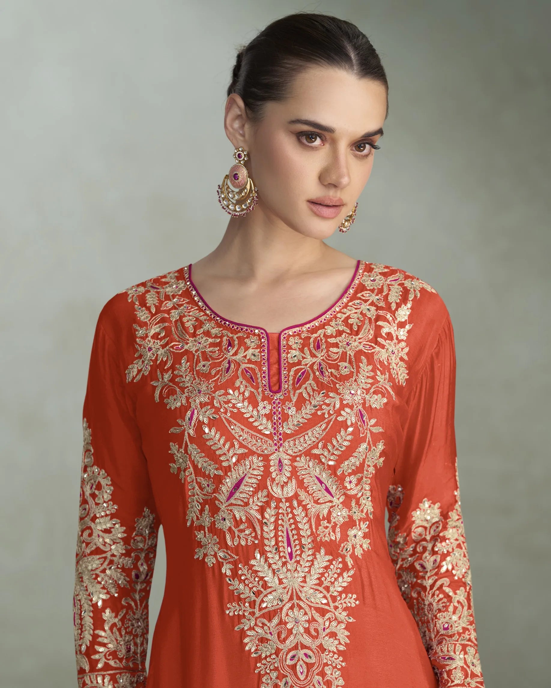 Woman wearing an orange embroidered dress with a neutral background