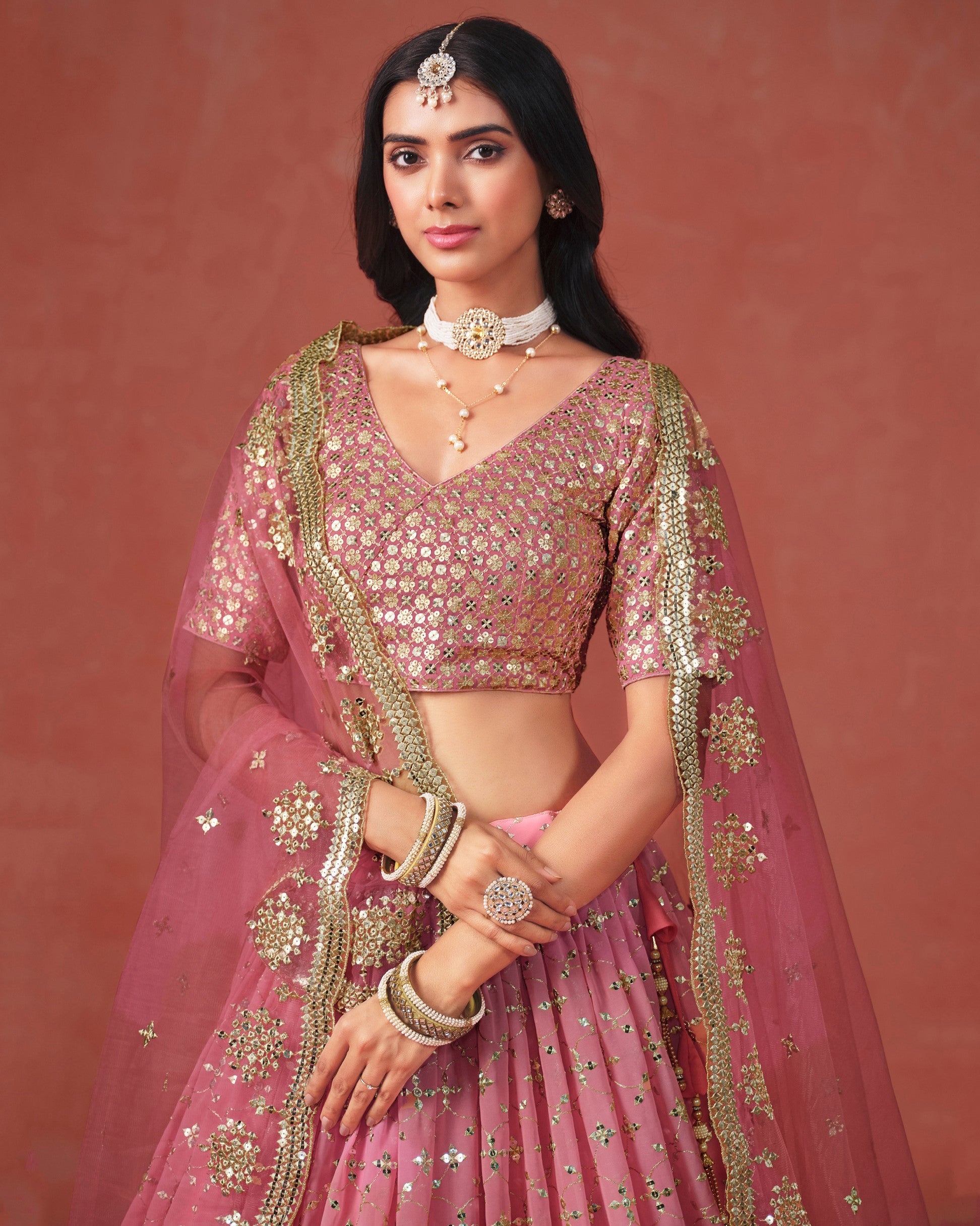 Woman in a traditional pink and gold outfit with jewelry against a red background