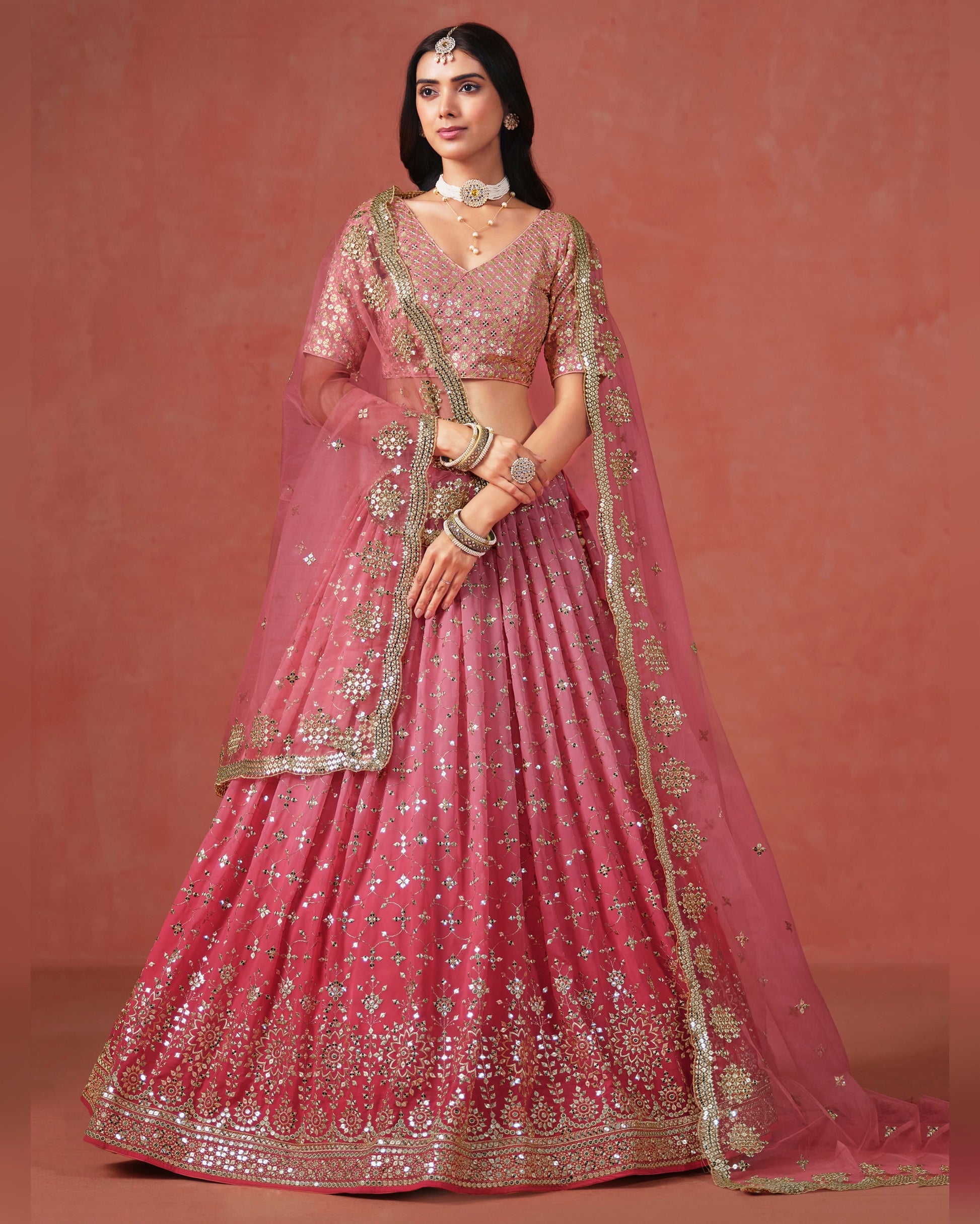 Woman wearing a pink embroidered lehenga with gold details on a matching background