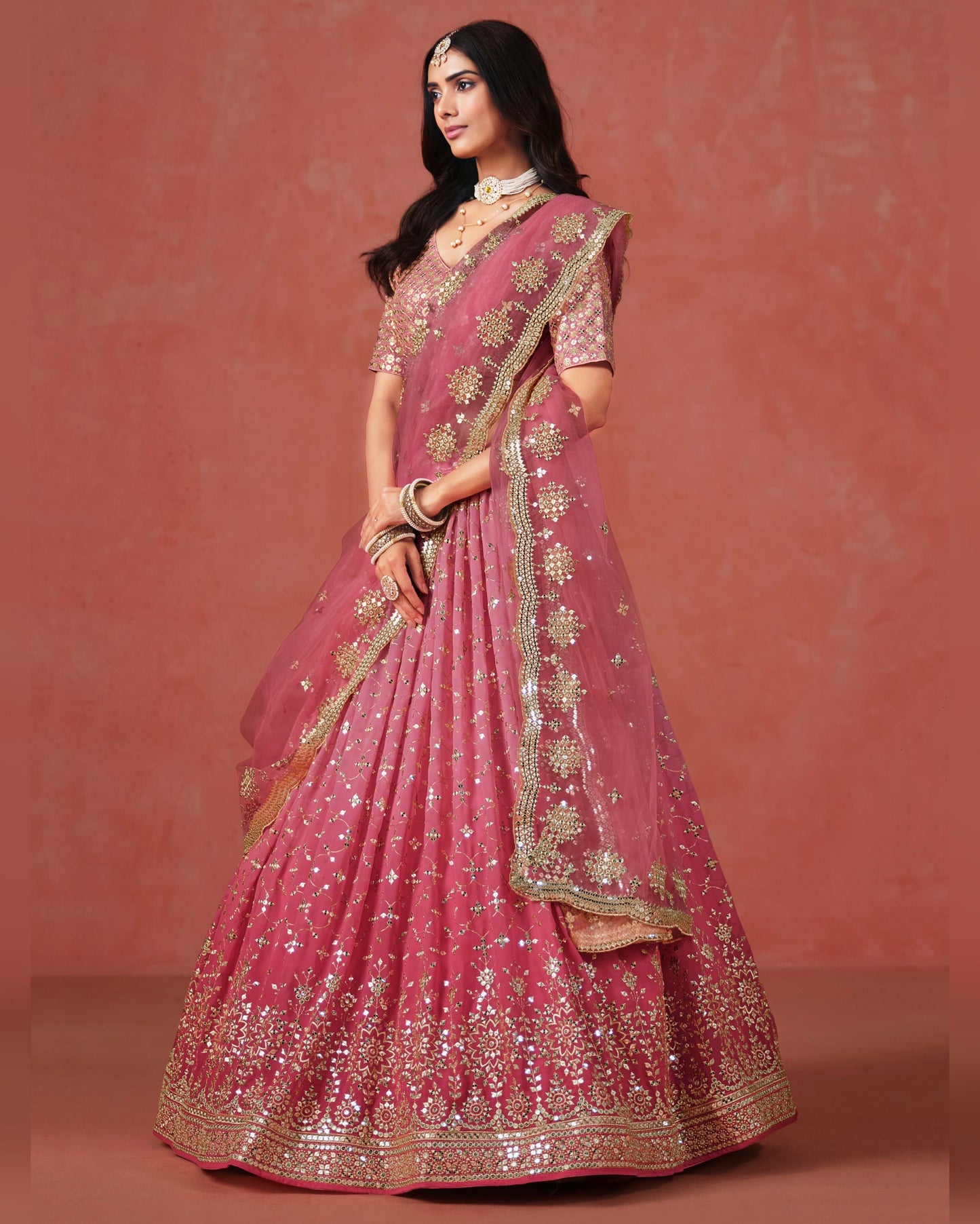 Woman wearing a pink embroidered traditional outfit against a matching background
