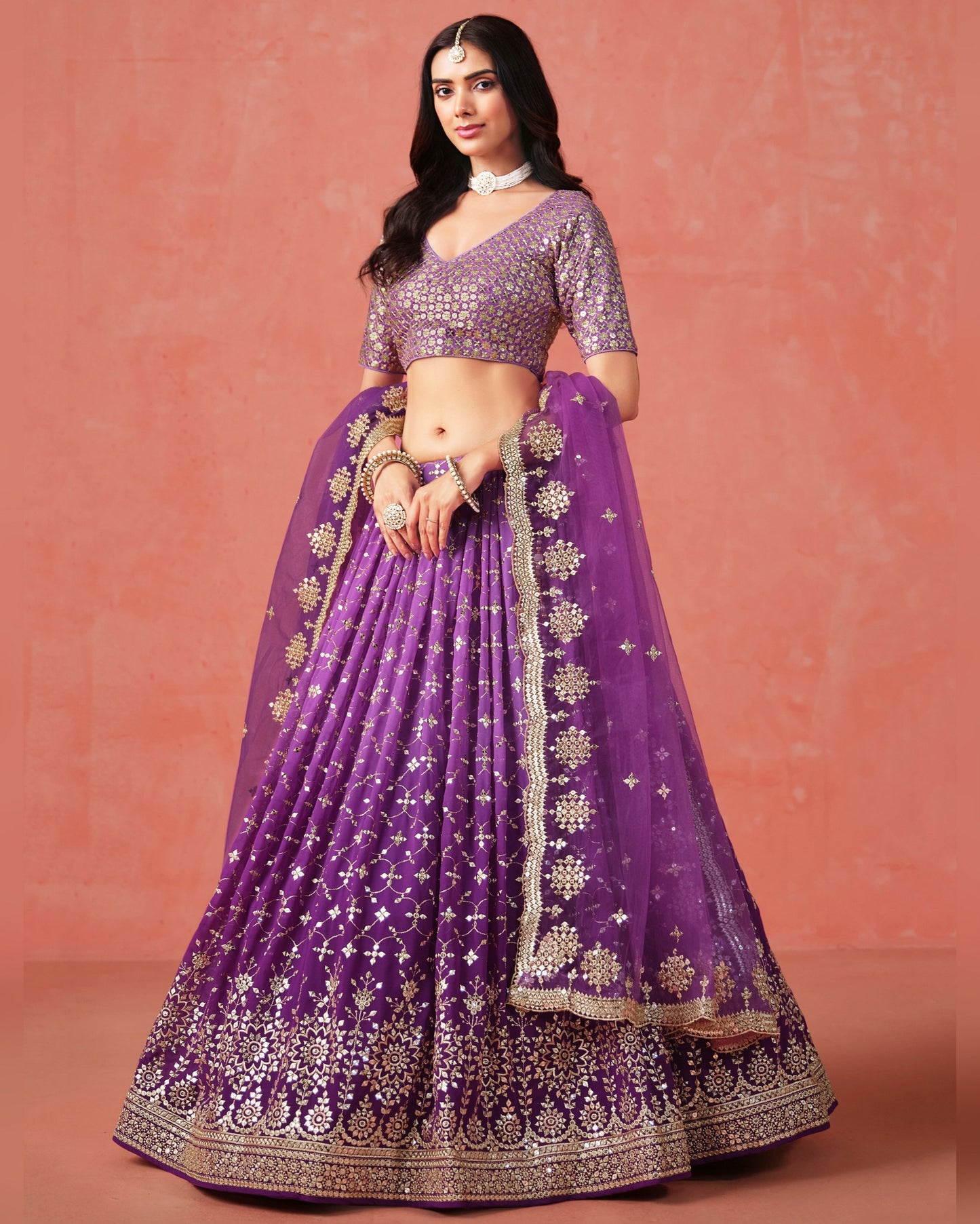 Woman wearing a purple embroidered traditional outfit on a pink background