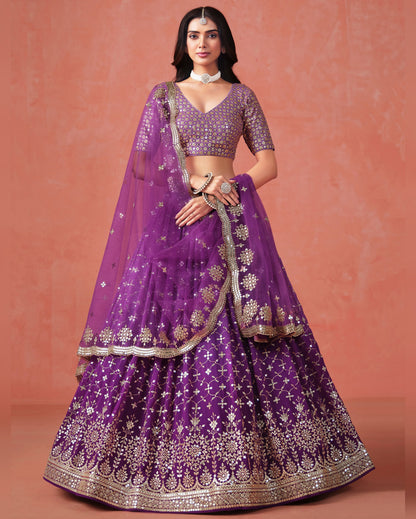 Woman wearing a purple embroidered lehenga with gold details on a pink background