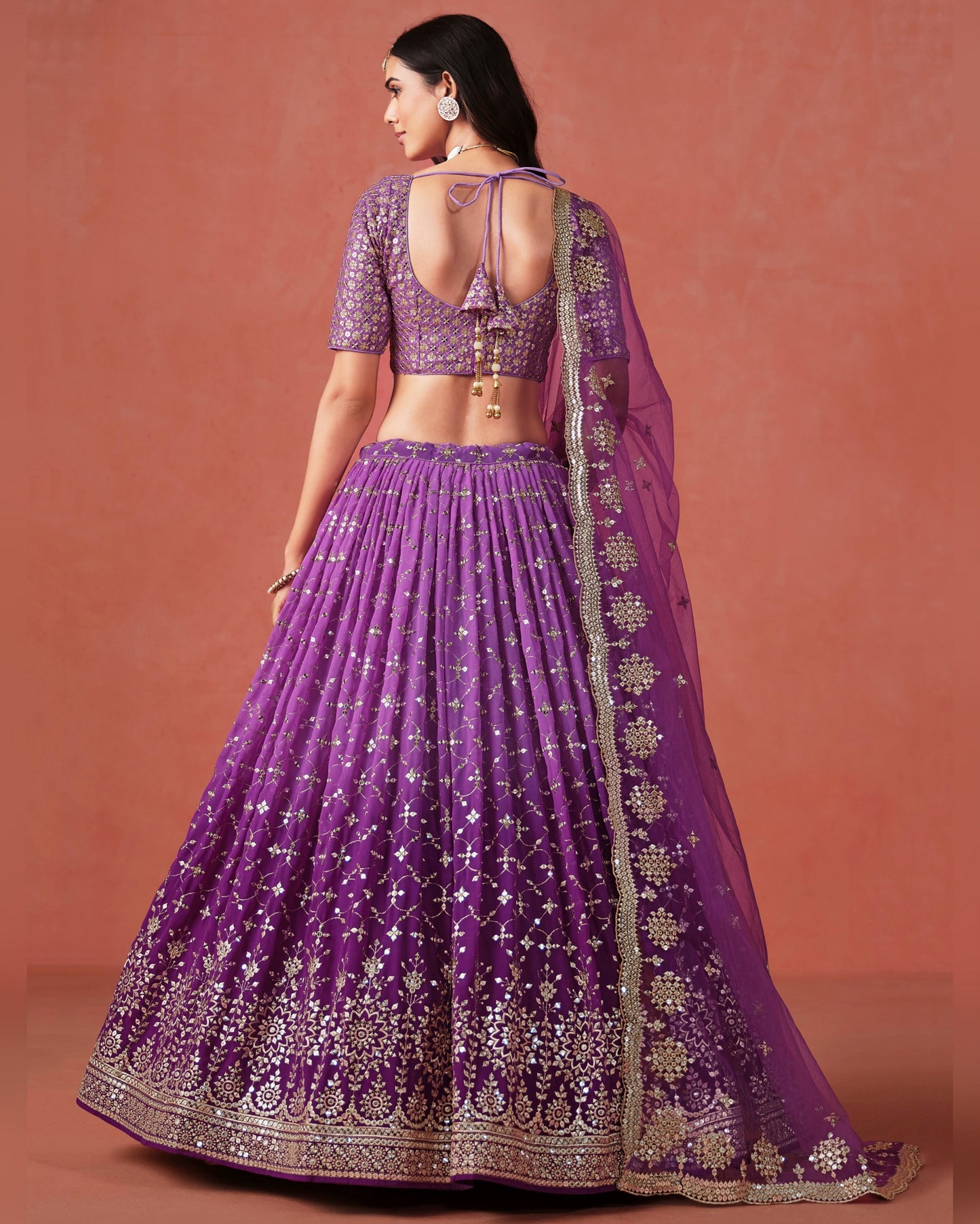 Purple embroidered traditional outfit on a model against a pinkish-brown background