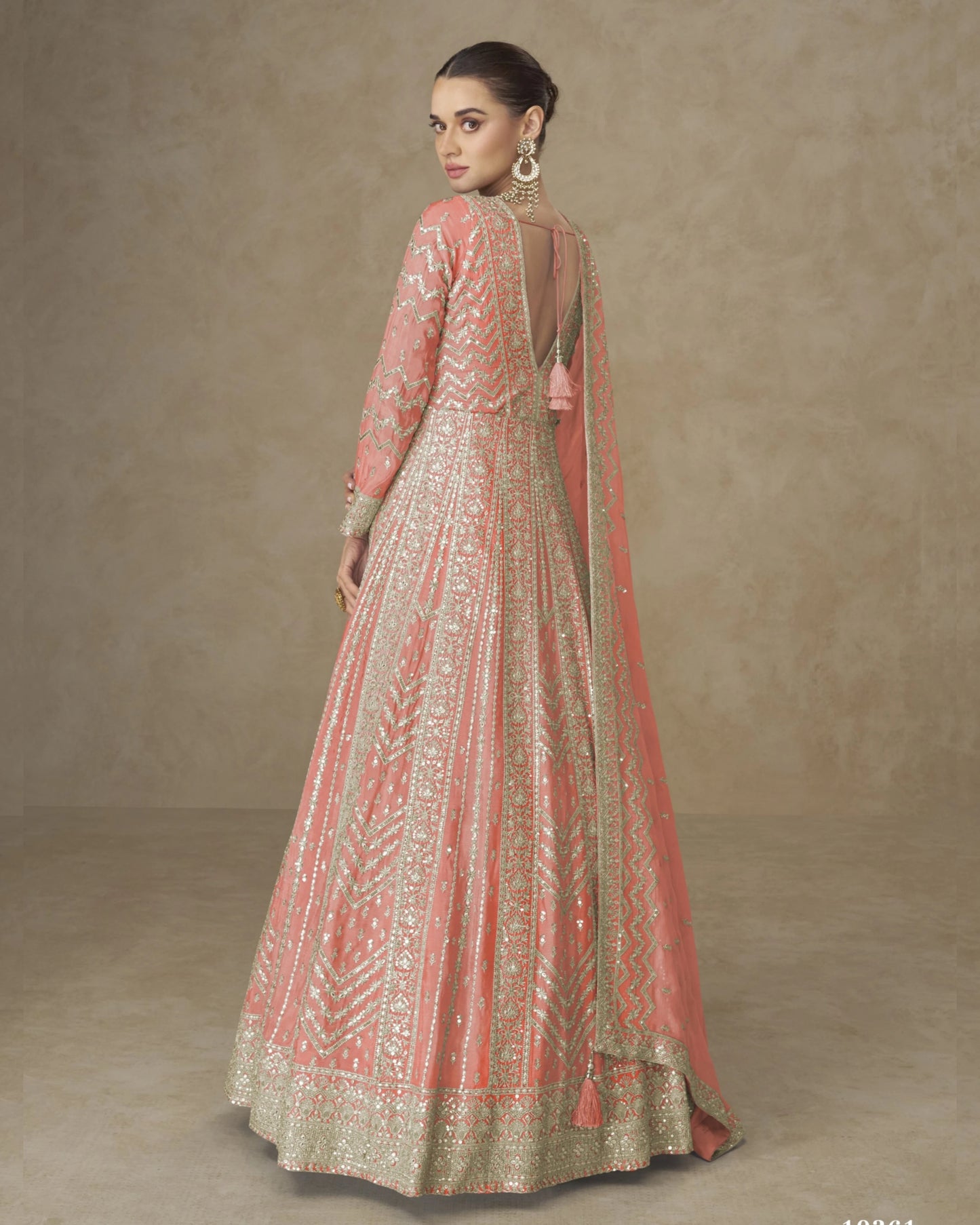 Woman wearing a traditional embroidered pink and gold dress against a beige background