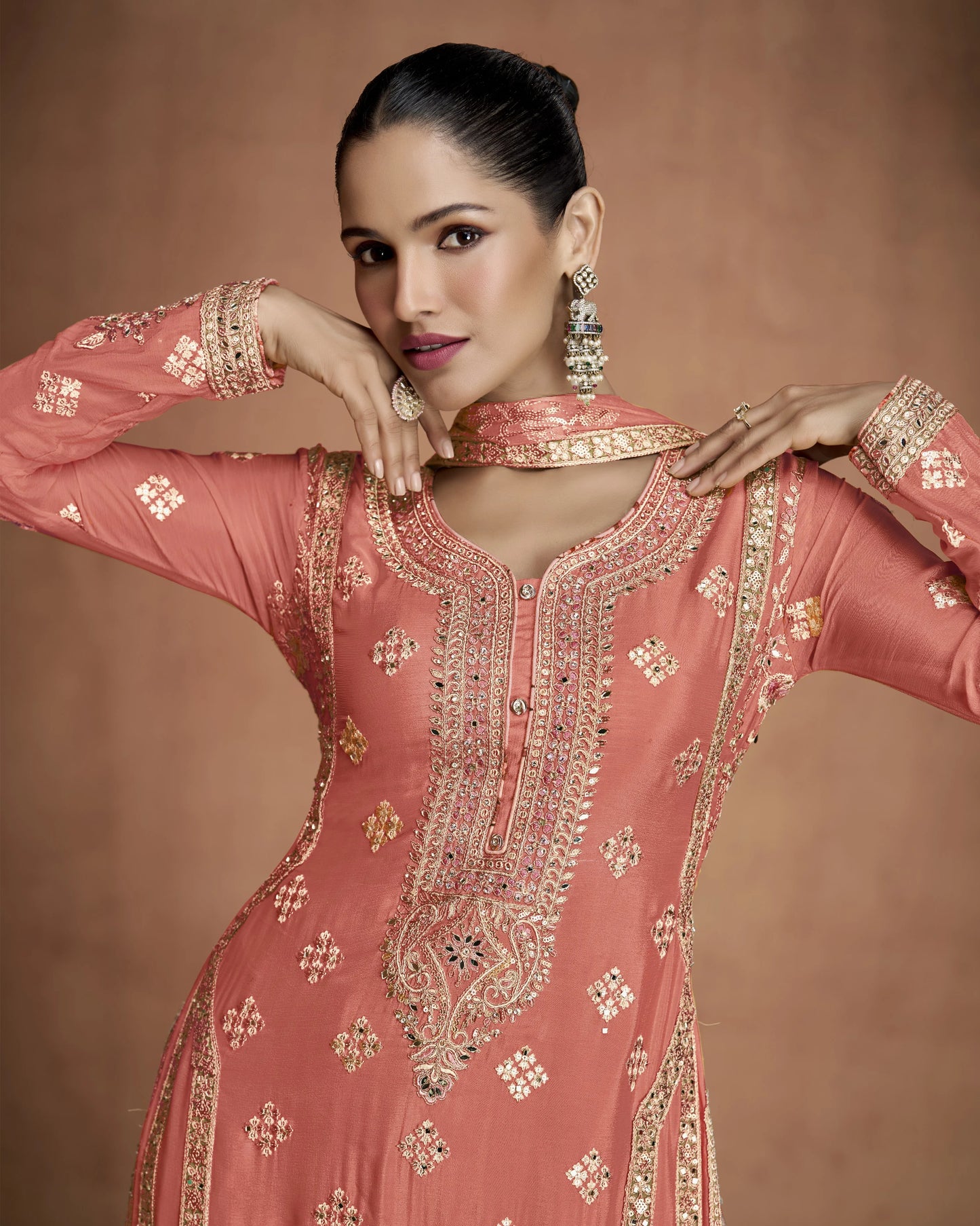Woman wearing a pink embroidered traditional outfit with gold jewelry against a brown background