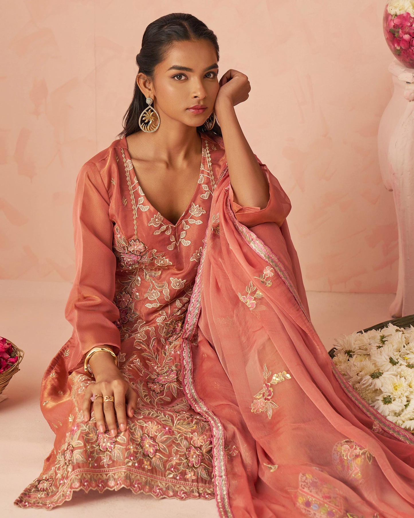 Woman in a traditional pink embroidered outfit with a matching dupatta against a pink background.