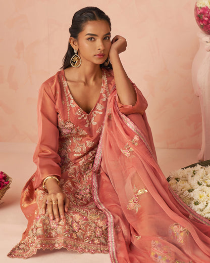 Woman in a traditional pink embroidered outfit with a matching dupatta against a pink background.