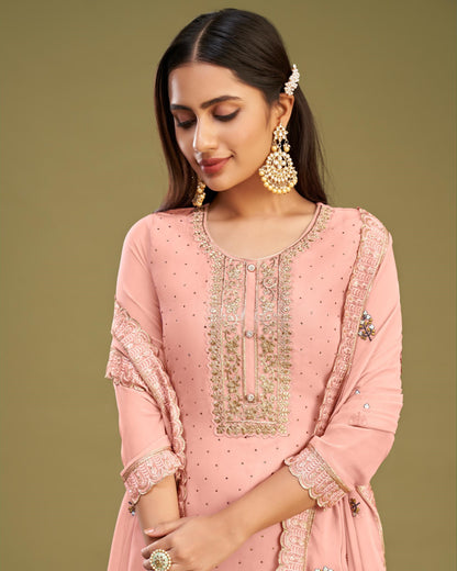 Woman wearing a pink embroidered traditional outfit with gold jewelry on a green background
