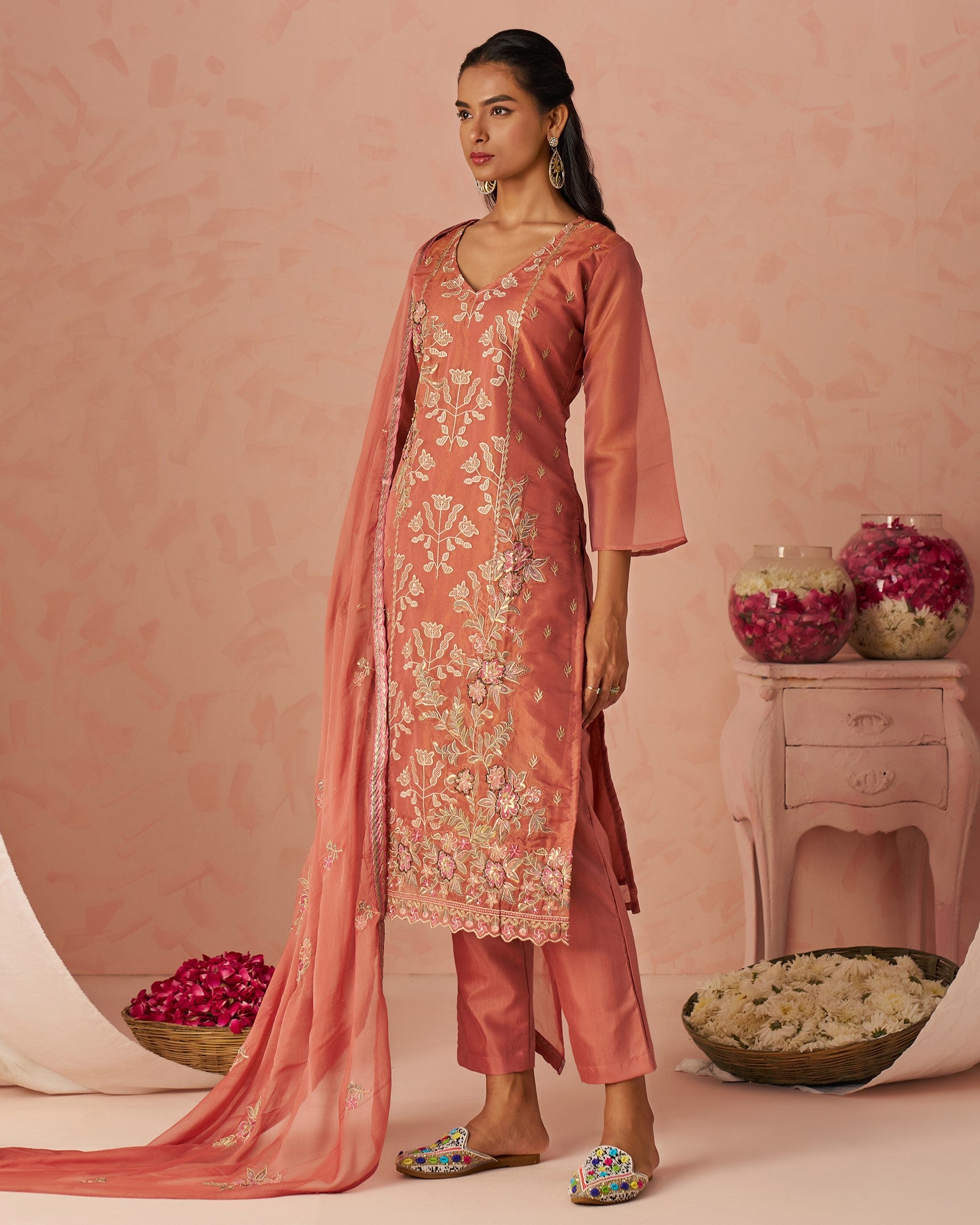 Woman in a traditional pink embroidered outfit with a matching dupatta against a pink background.