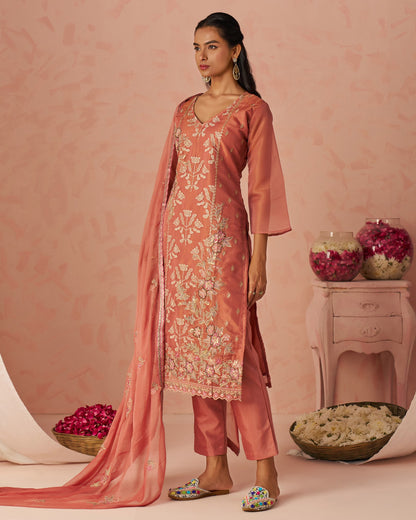 Woman in a traditional pink embroidered outfit with a matching dupatta against a pink background.