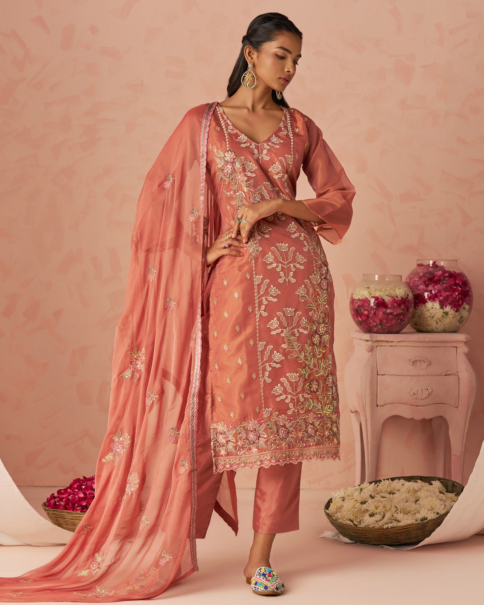 Woman in a traditional pink embroidered outfit with a matching dupatta against a pink background.