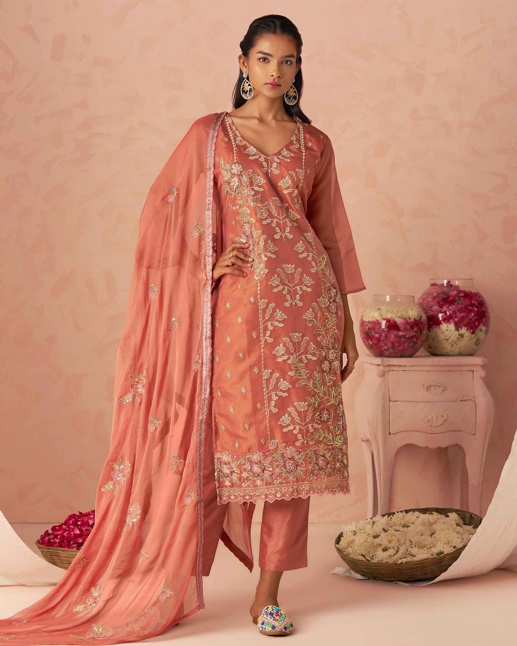 Woman in a traditional pink embroidered outfit with a matching dupatta against a pink background.