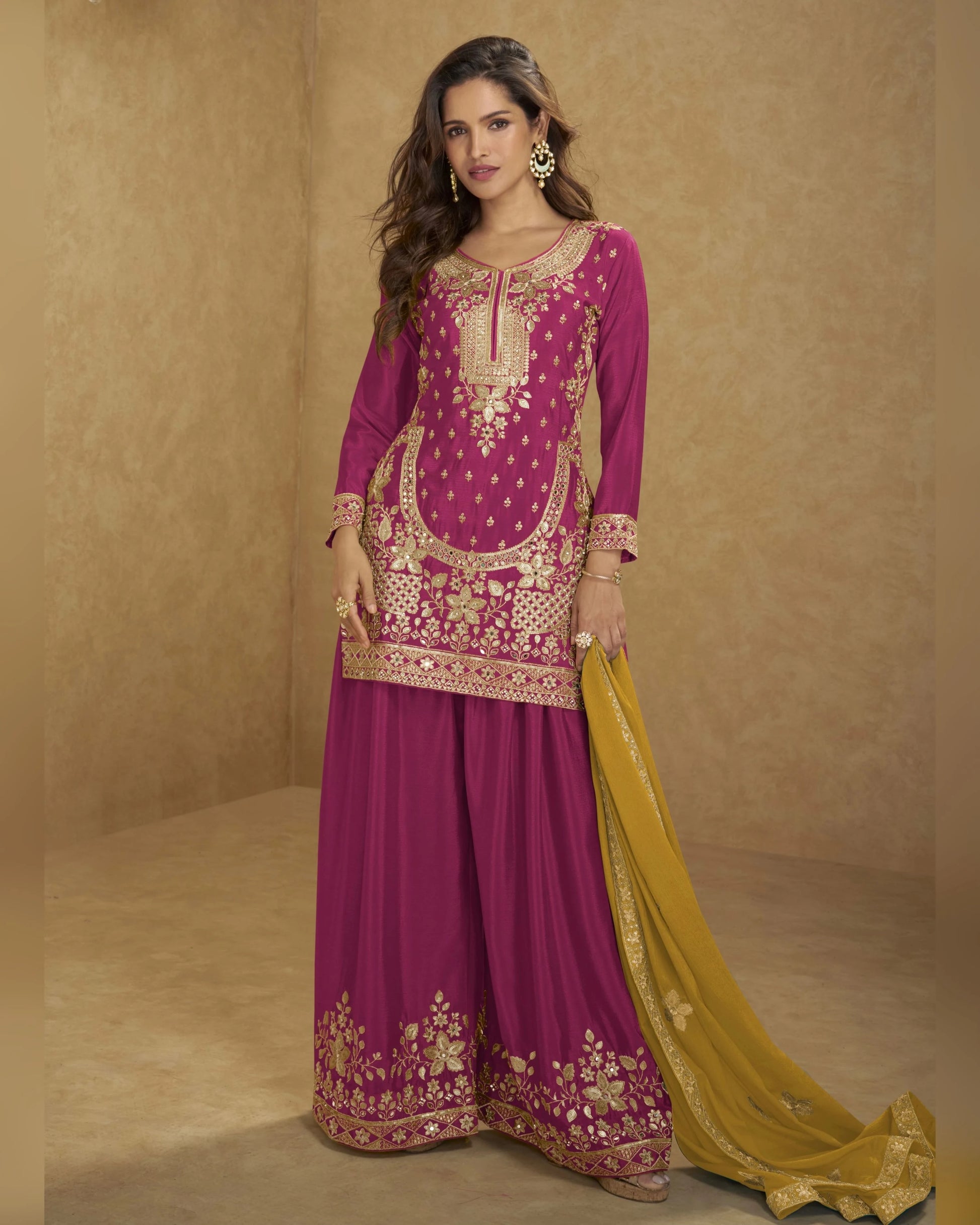 Woman wearing a traditional pink and gold embroidered outfit with a yellow dupatta on a beige background