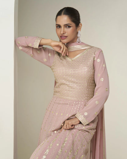 Woman wearing a pink and gold traditional outfit against a plain background