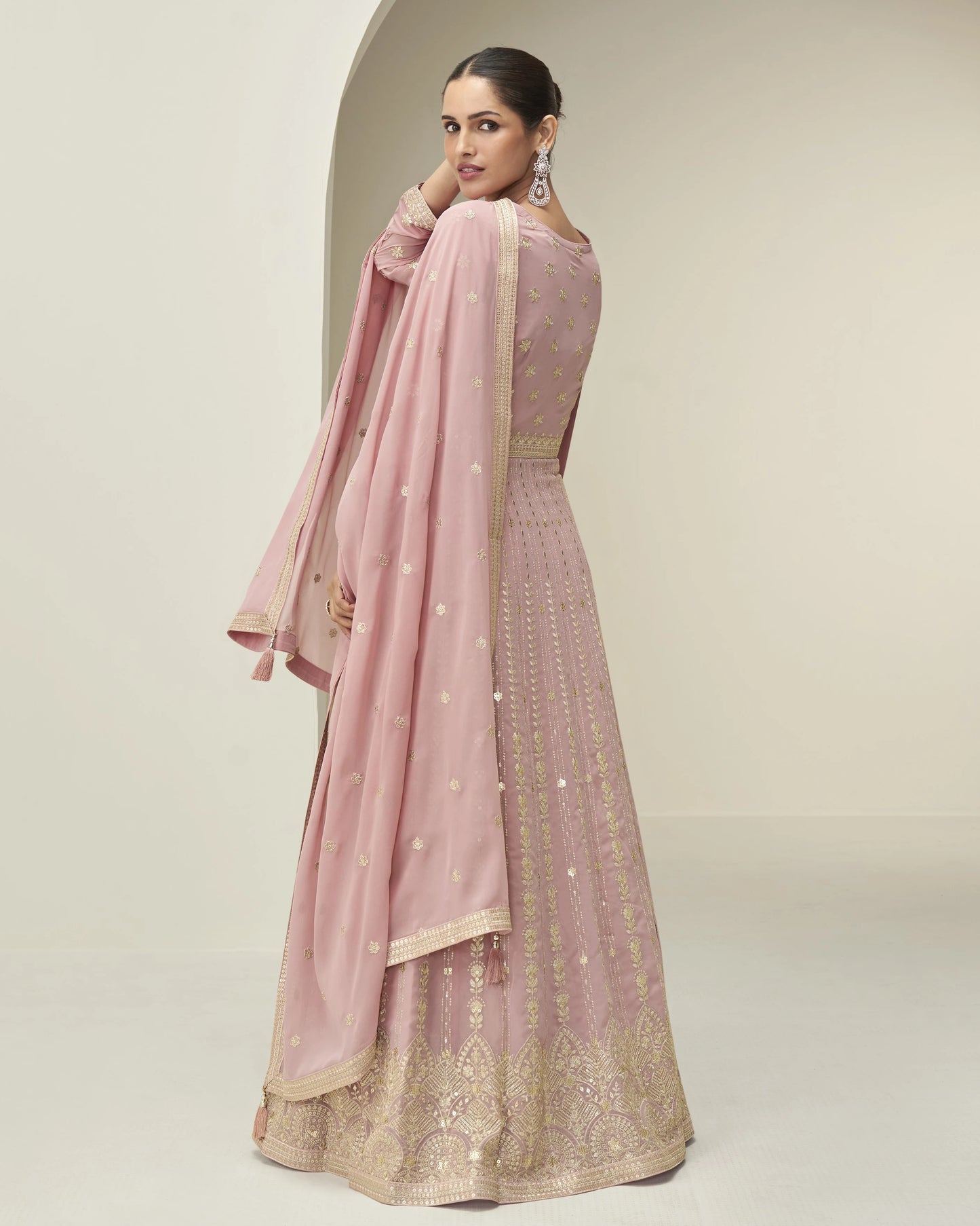 Woman wearing a pink traditional outfit with gold embroidery on a beige background