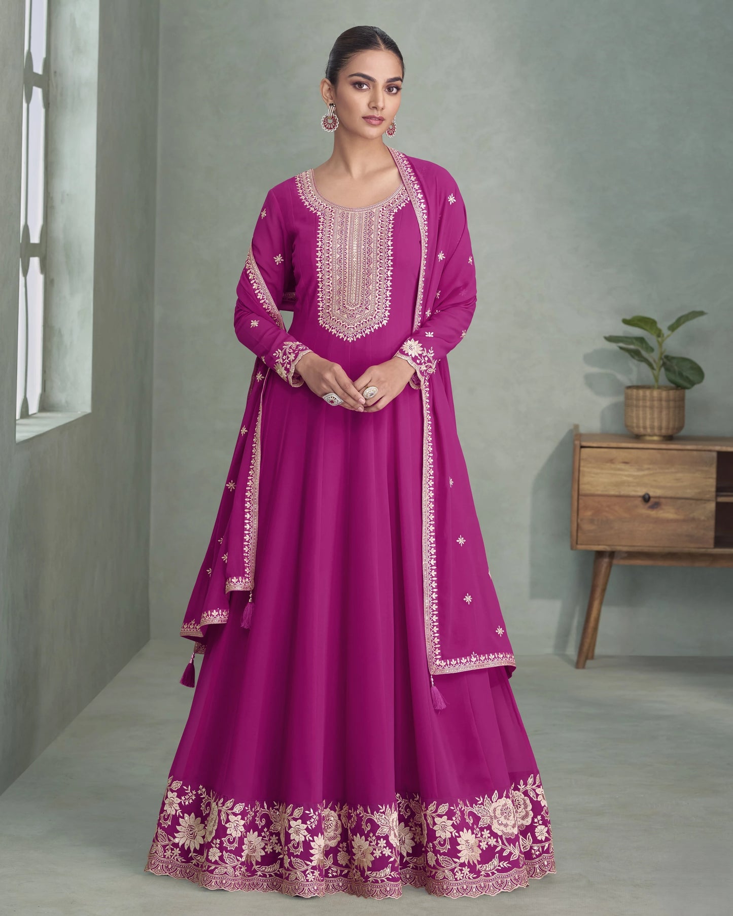 Woman wearing a magenta traditional outfit with white embroidery in a minimalistic room.