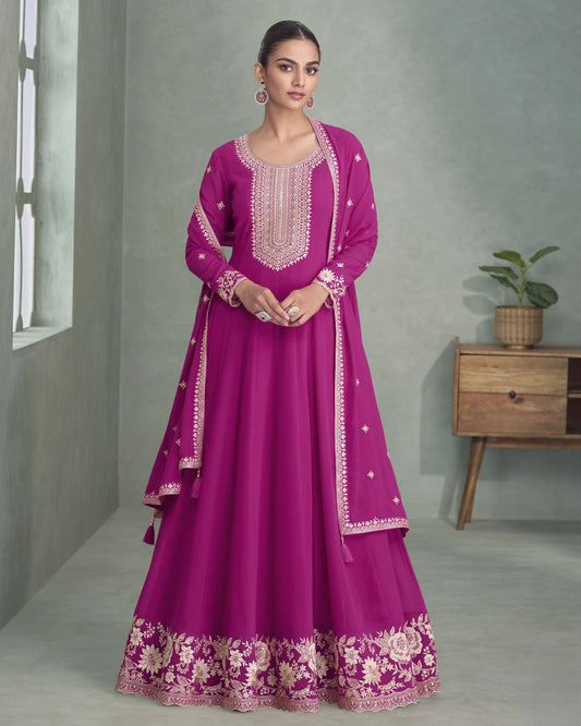 Woman wearing a magenta traditional outfit with white embroidery in a minimalistic room.