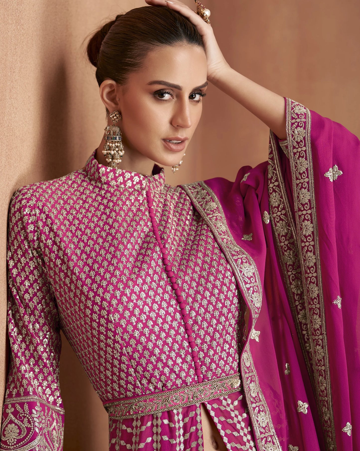 Woman wearing a traditional pink and gold outfit with a matching dupatta against a beige background