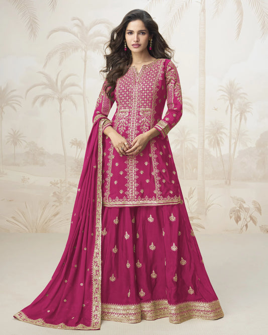 Woman wearing a pink embroidered traditional outfit with a matching dupatta against a decorative white background.