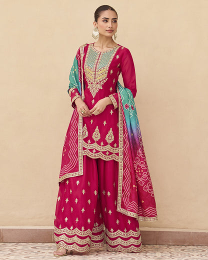 Woman wearing a traditional pink and green embroidered outfit against a beige background
