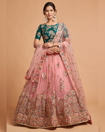 Woman wearing a traditional embroidered outfit with a green blouse and pink lehenga on a beige background