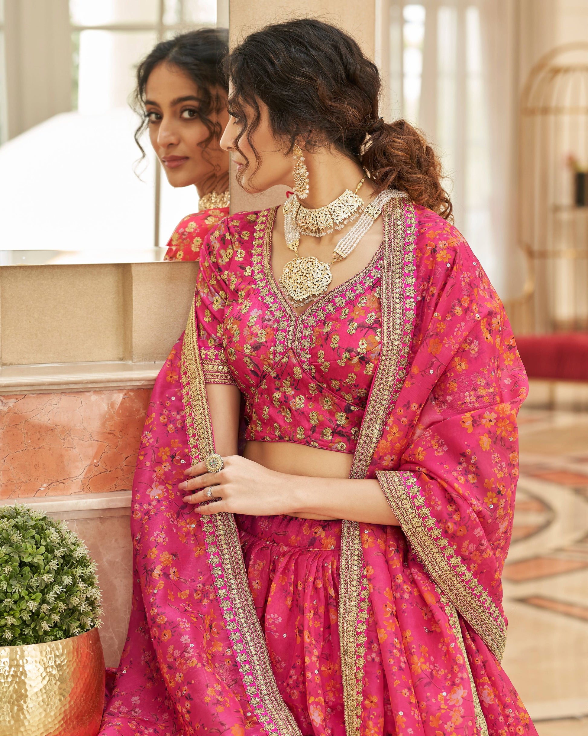 Woman in a pink traditional outfit with gold embroidery, standing indoors.