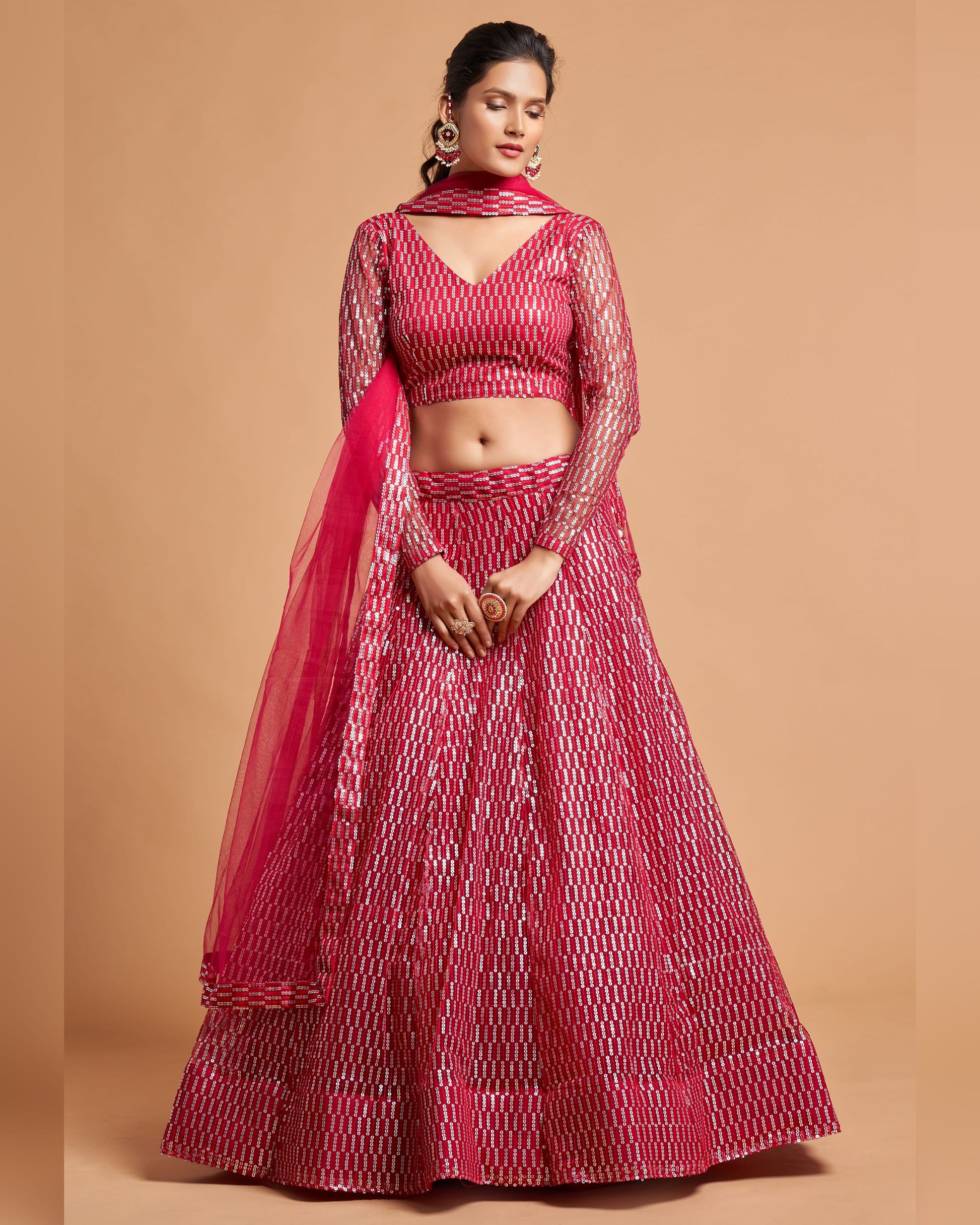Woman wearing a red and white patterned lehenga with a dupatta on a beige background