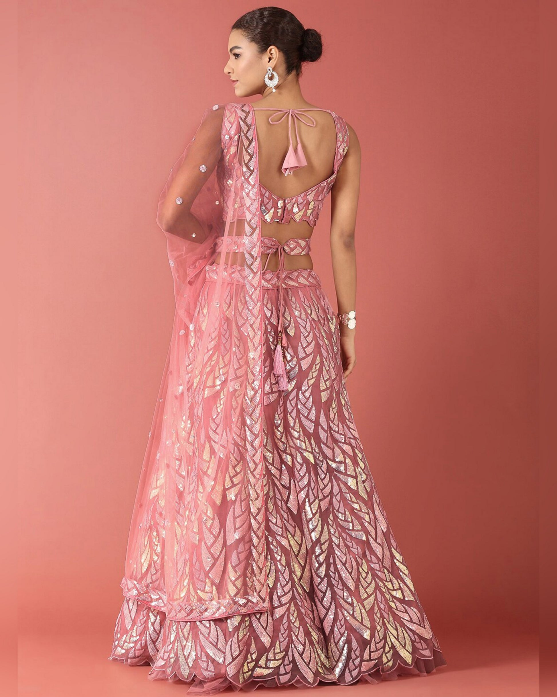 Woman wearing a pink and gold patterned saree against a pink background
