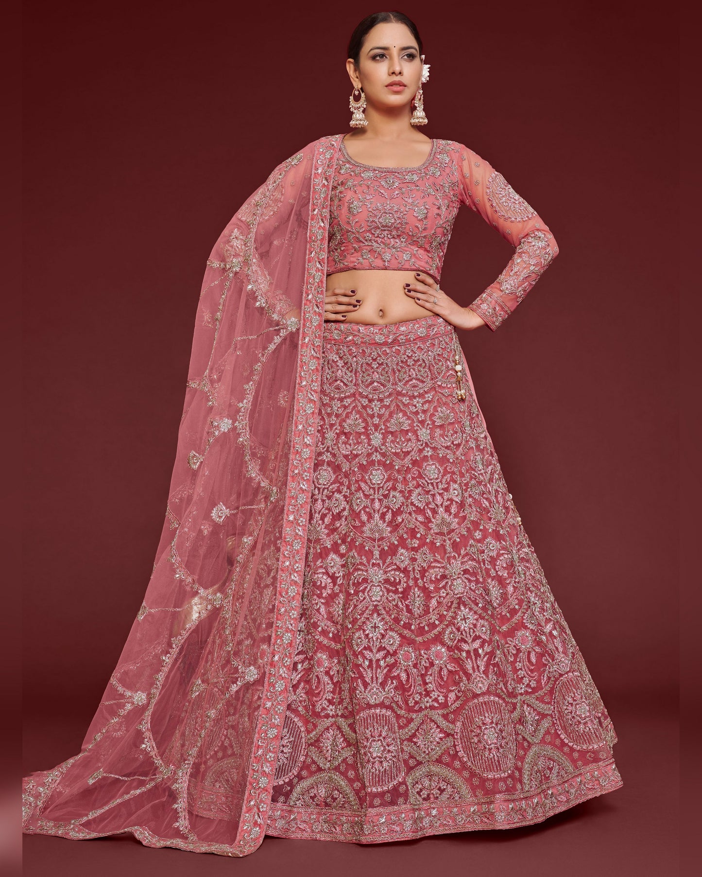 Woman wearing a pink embroidered lehenga with a matching blouse on a red background