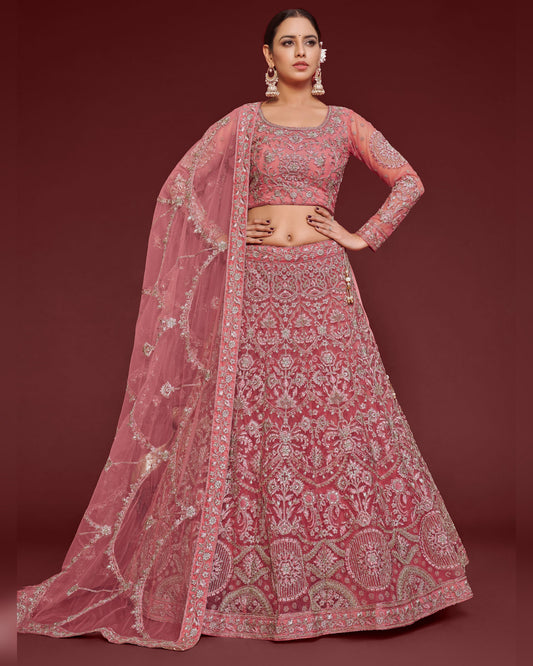 Woman wearing a pink embroidered lehenga with a matching blouse on a red background