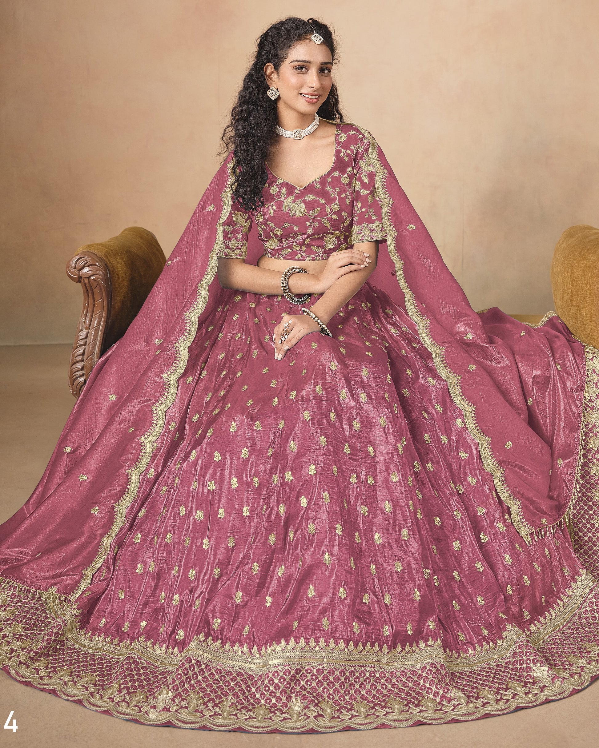 Woman wearing a traditional pink embroidered outfit with a gold border against a beige background