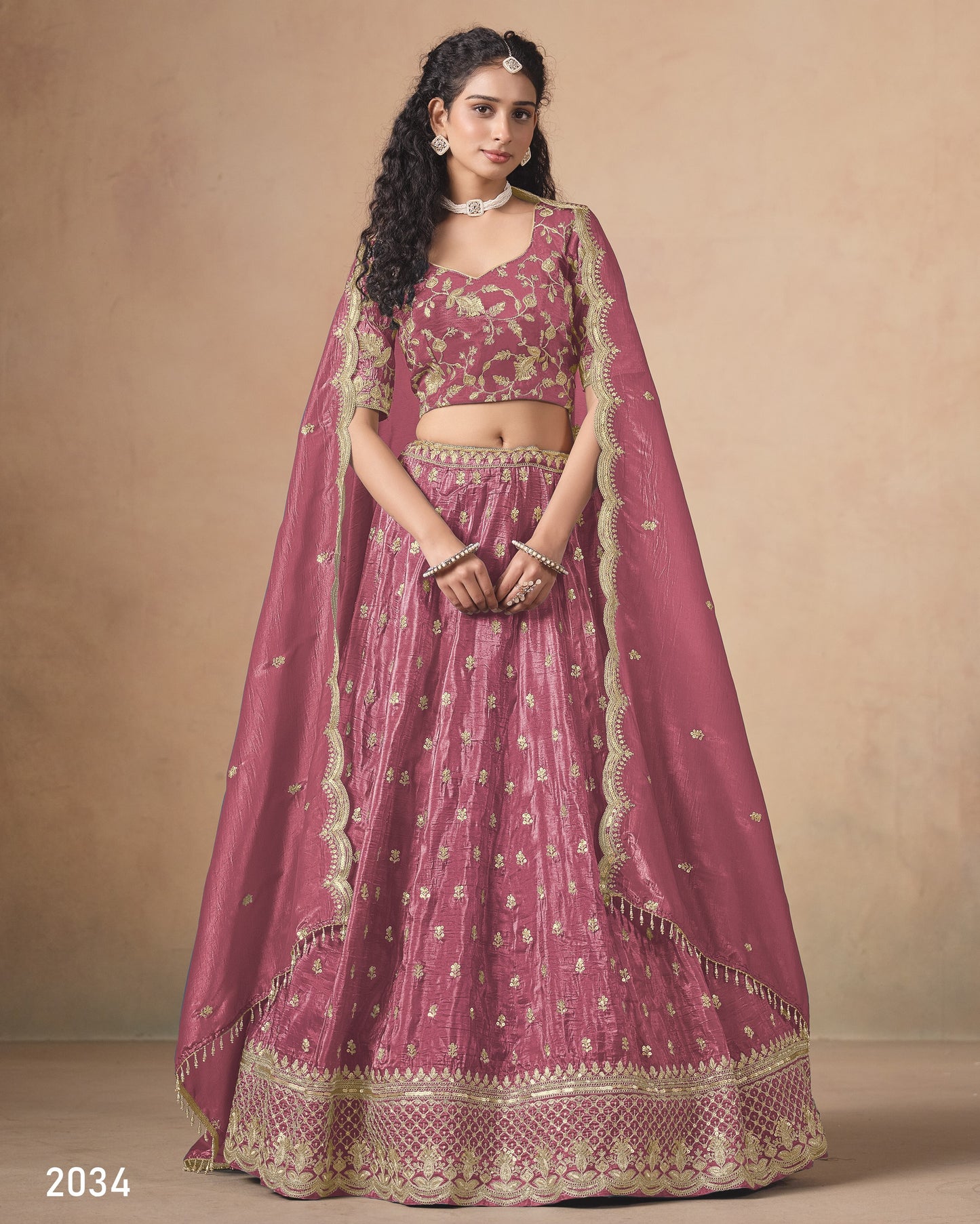 Woman wearing a traditional pink and gold embroidered lehenga on a beige background
