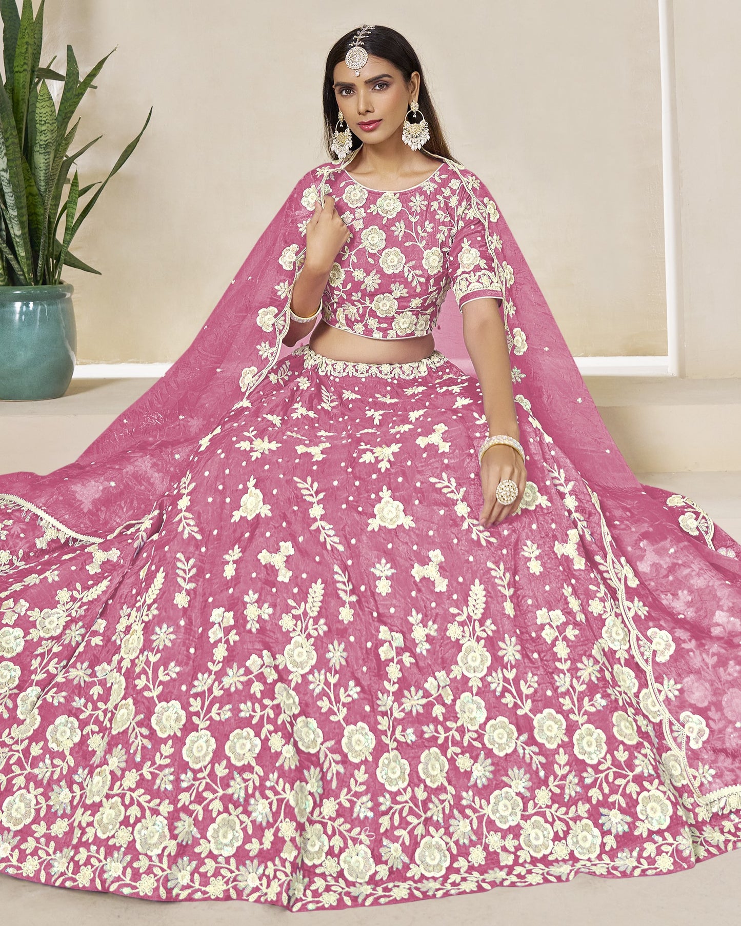 Woman wearing a pink floral lehenga with a matching dupatta in a minimal indoor setting.
