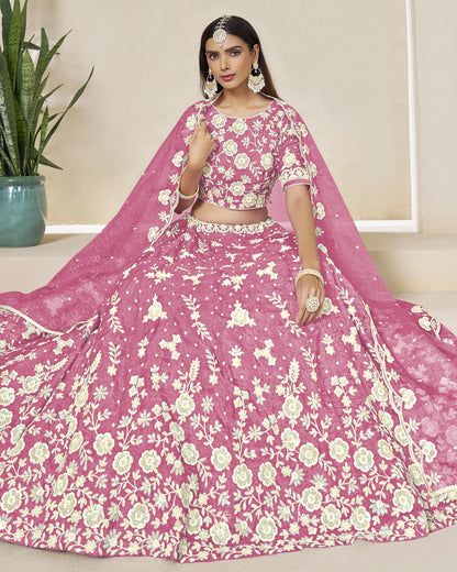 Woman wearing a pink floral lehenga with a matching dupatta in a minimal indoor setting.