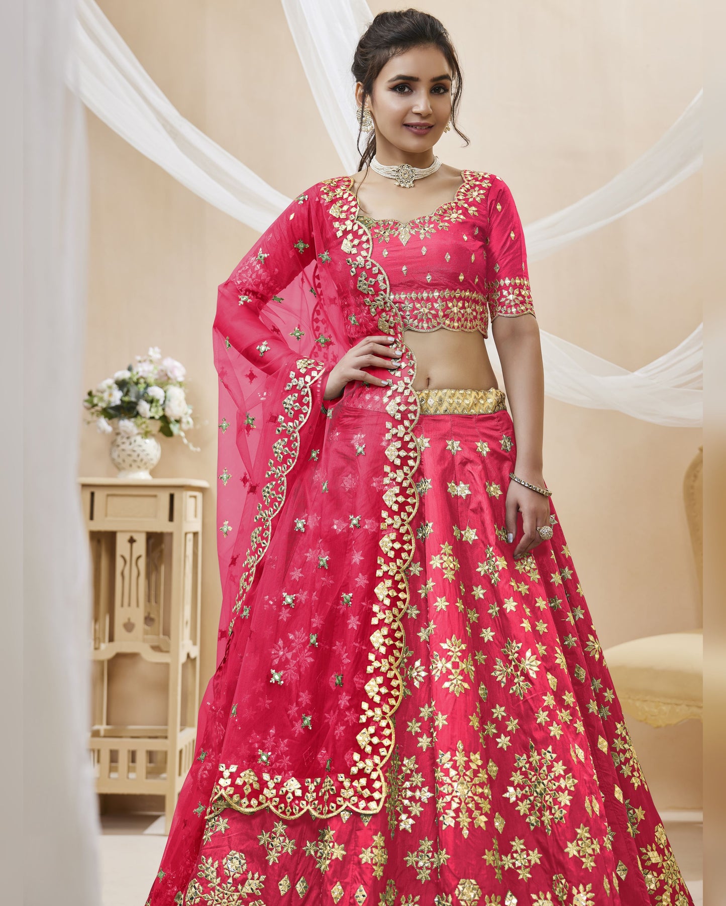 Woman wearing a pink embroidered saree with a gold blouse in a decorated room.