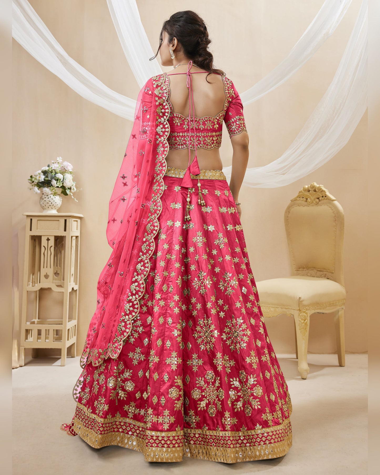 Woman wearing a pink and gold embroidered traditional outfit in a decorated room.