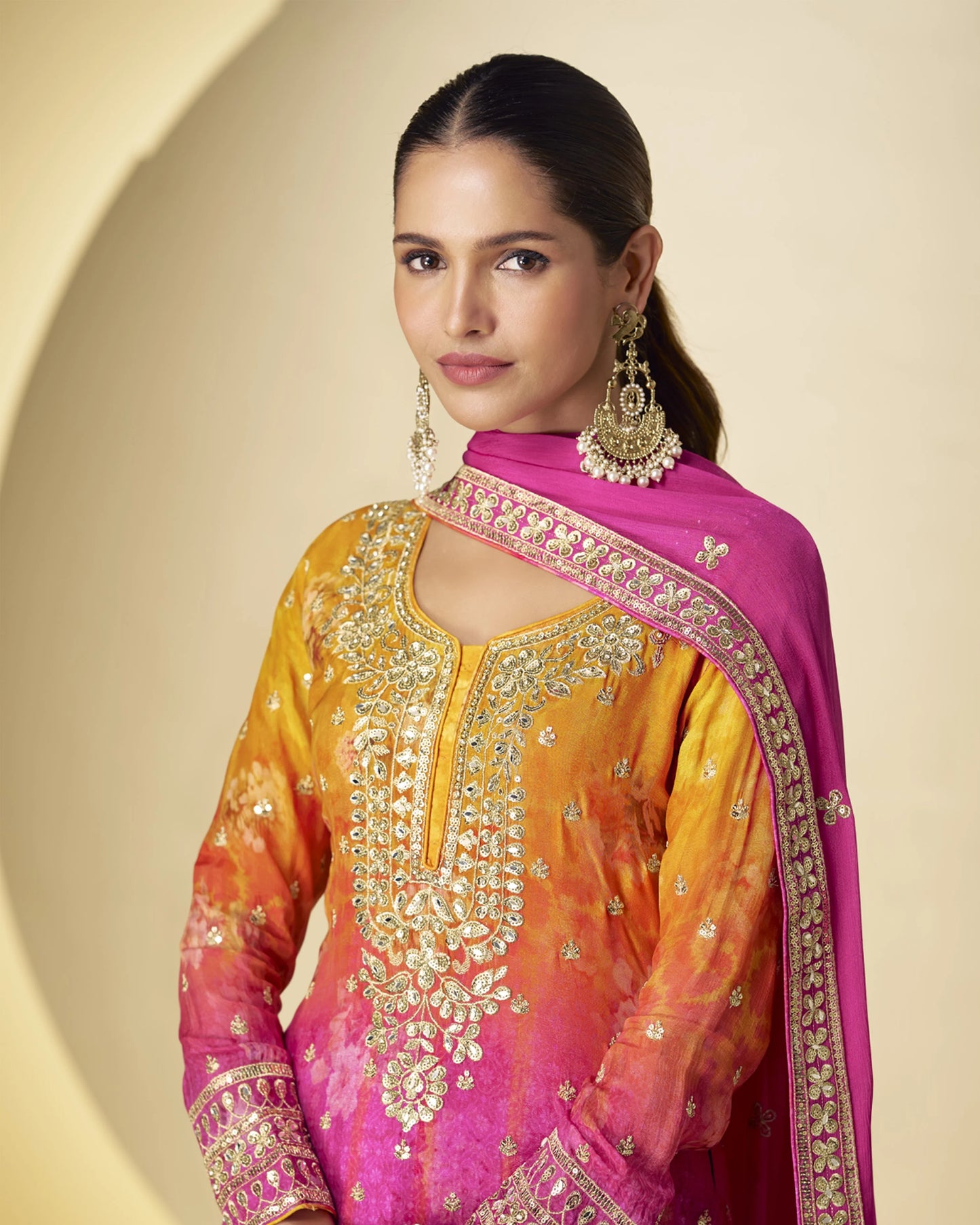 Woman wearing a traditional embroidered outfit with a pink dupatta on a beige background