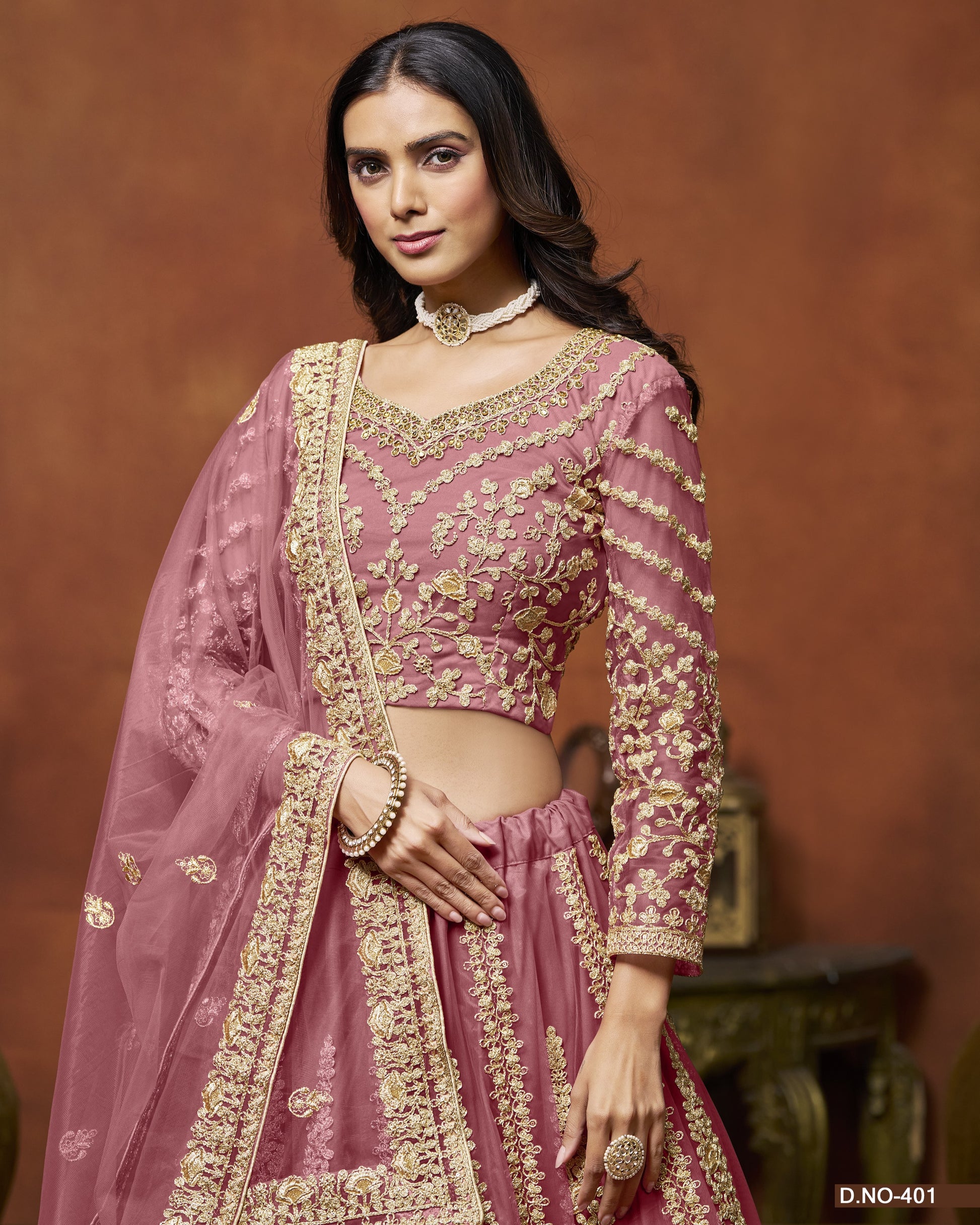 Woman wearing a traditional pink and gold embroidered outfit against a brown background