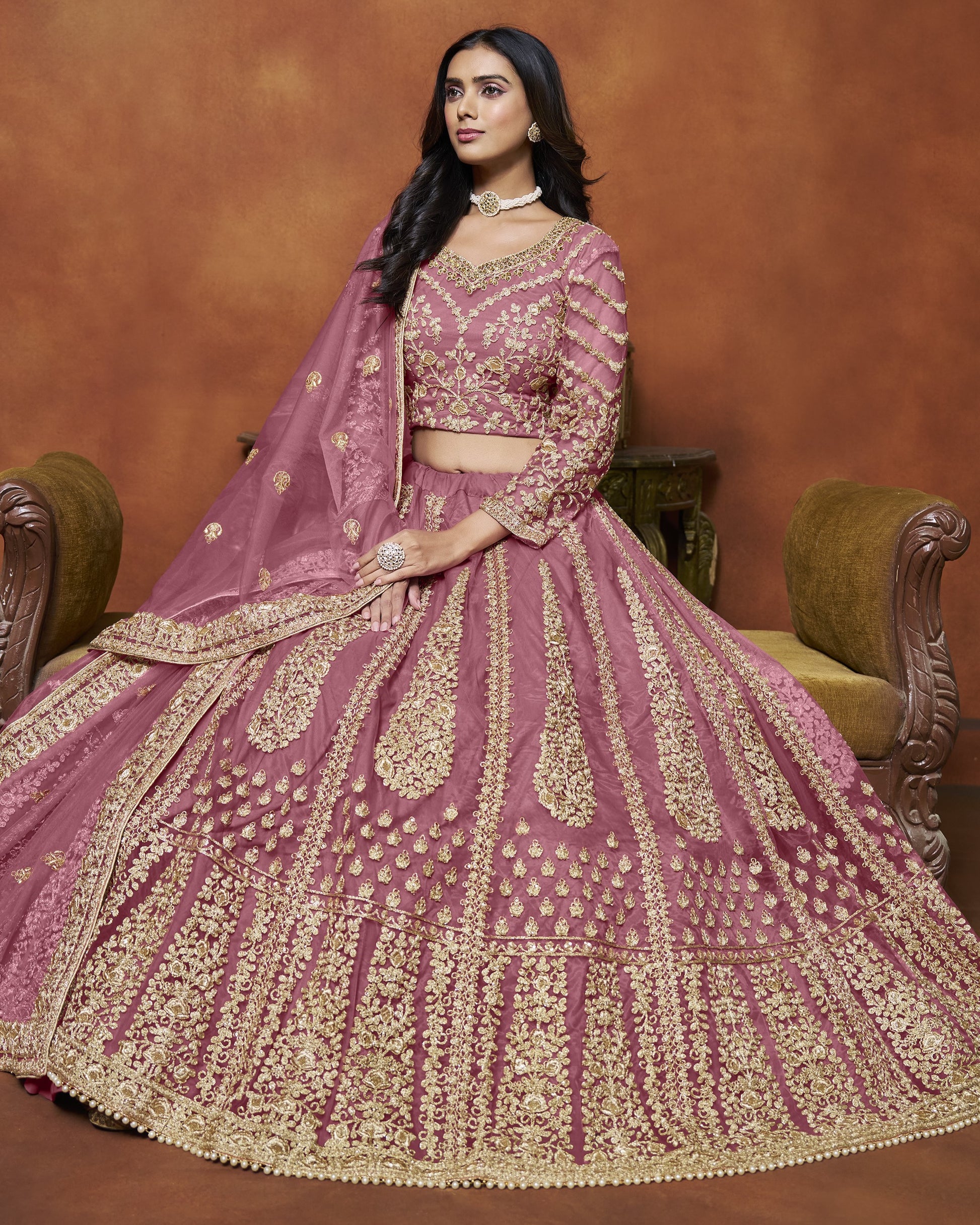 Woman in a traditional pink and gold embroidered outfit against a brown background