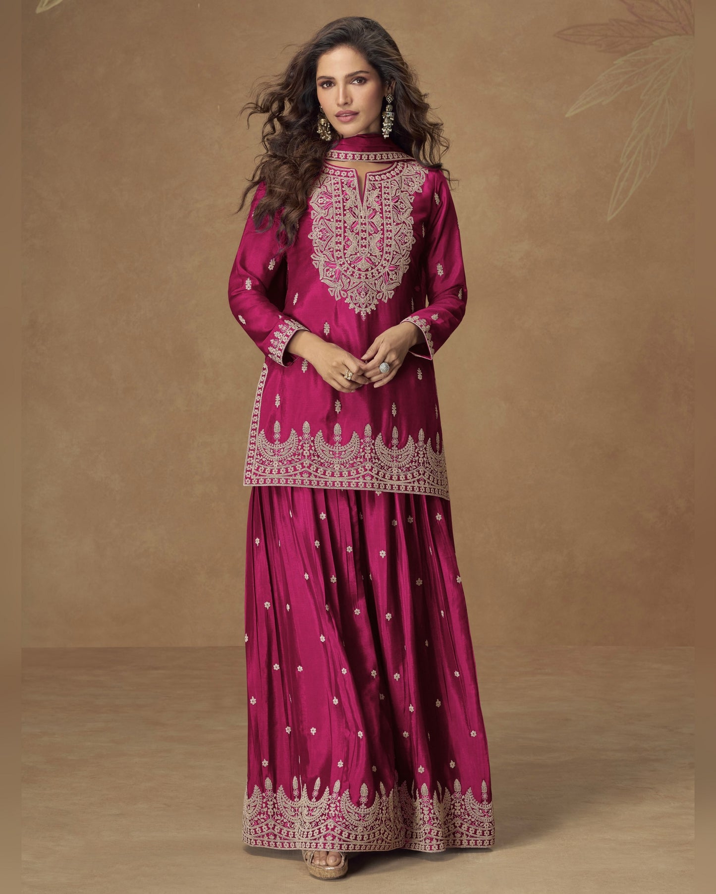 Woman wearing a pink traditional outfit with intricate embroidery on a brown background