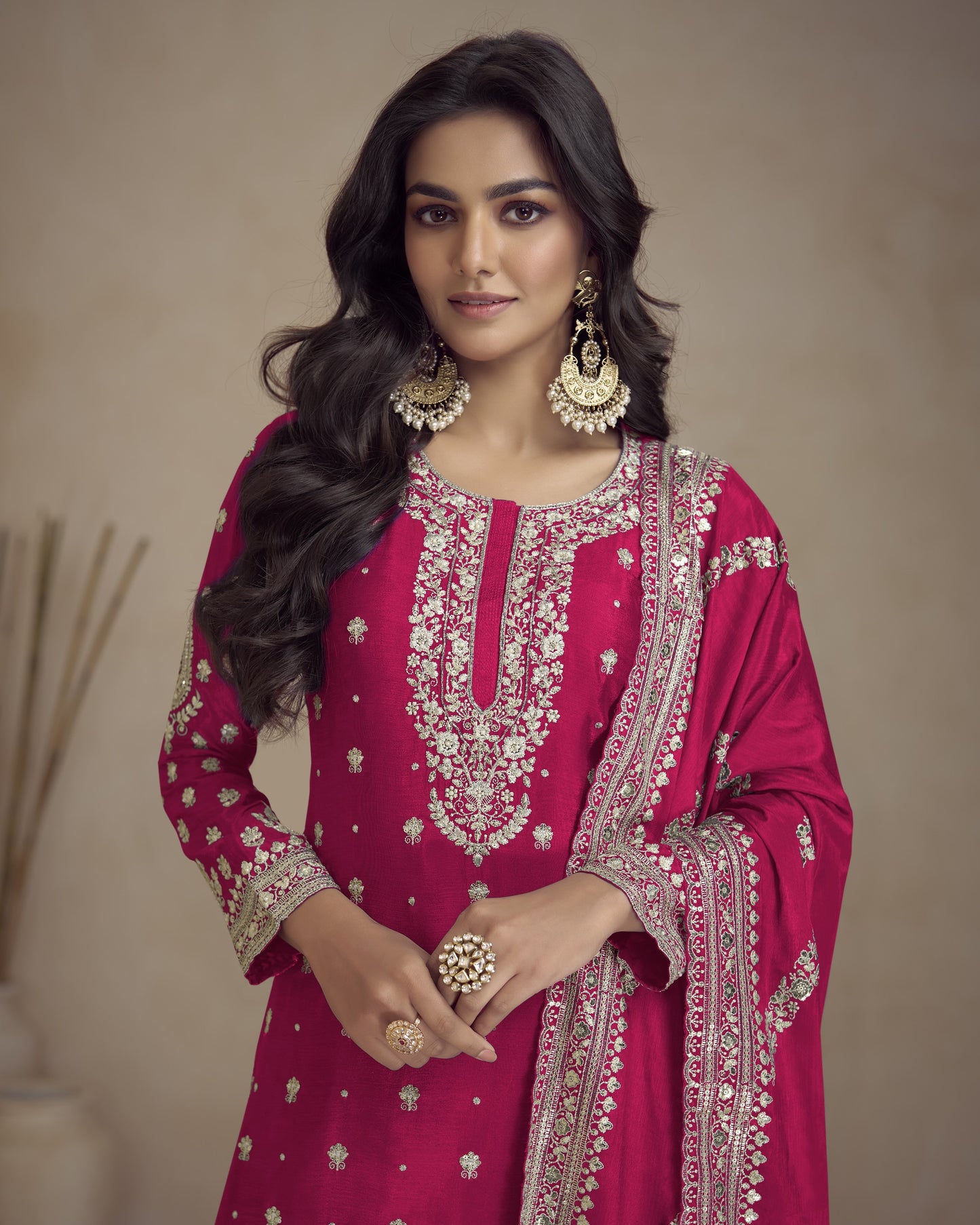 Woman wearing a pink embroidered traditional outfit with gold jewelry against a neutral background